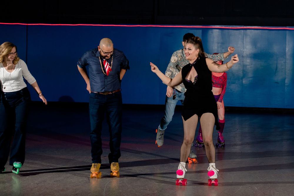 Roller skaters practice dance moves on a rink with colorful walls in the background.