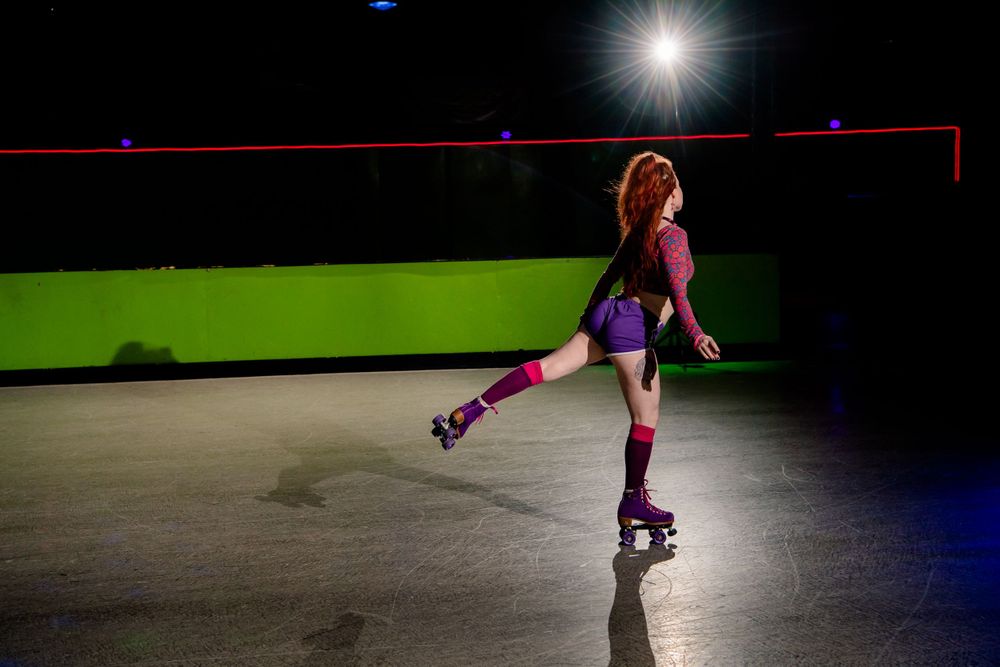 Solo roller skater performs under dramatic lighting against green and blue walls.