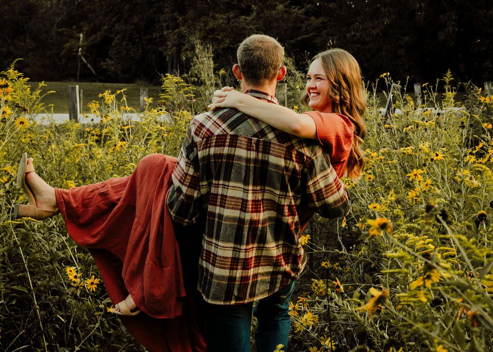 Guy carries girl through wild flower patch at a local park