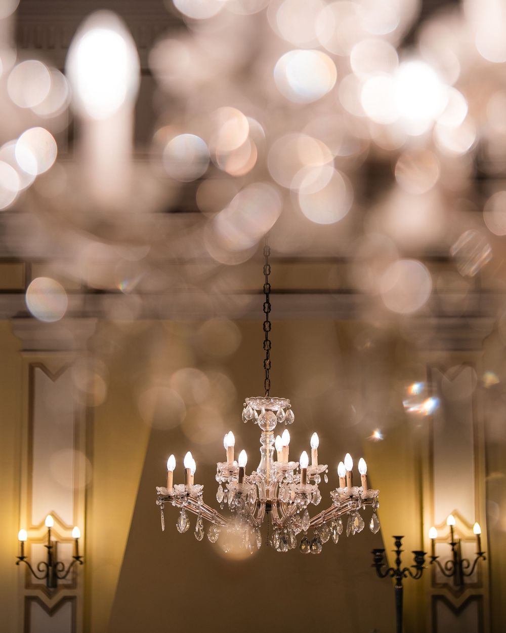 Crystal chandelier hanging in an elegant room with soft bokeh lights and wall sconces creating a warm ambiance.
