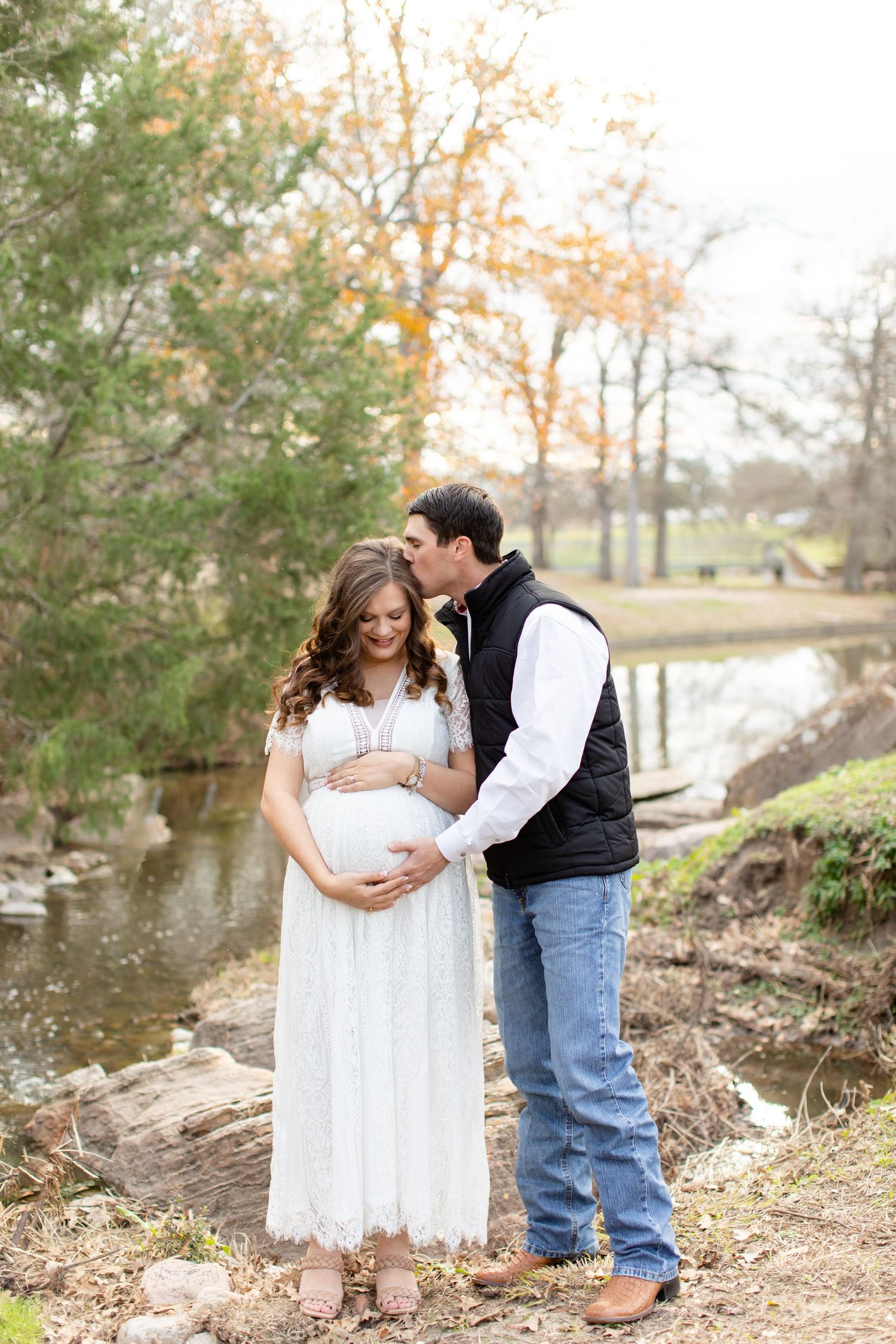 A couple poses for maternity photos by a peaceful stream in autumn.