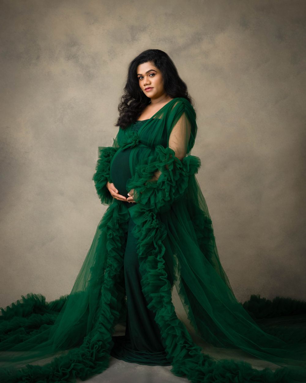 Elegant maternity portrait featuring a flowing emerald green tulle gown against a muted backdrop.