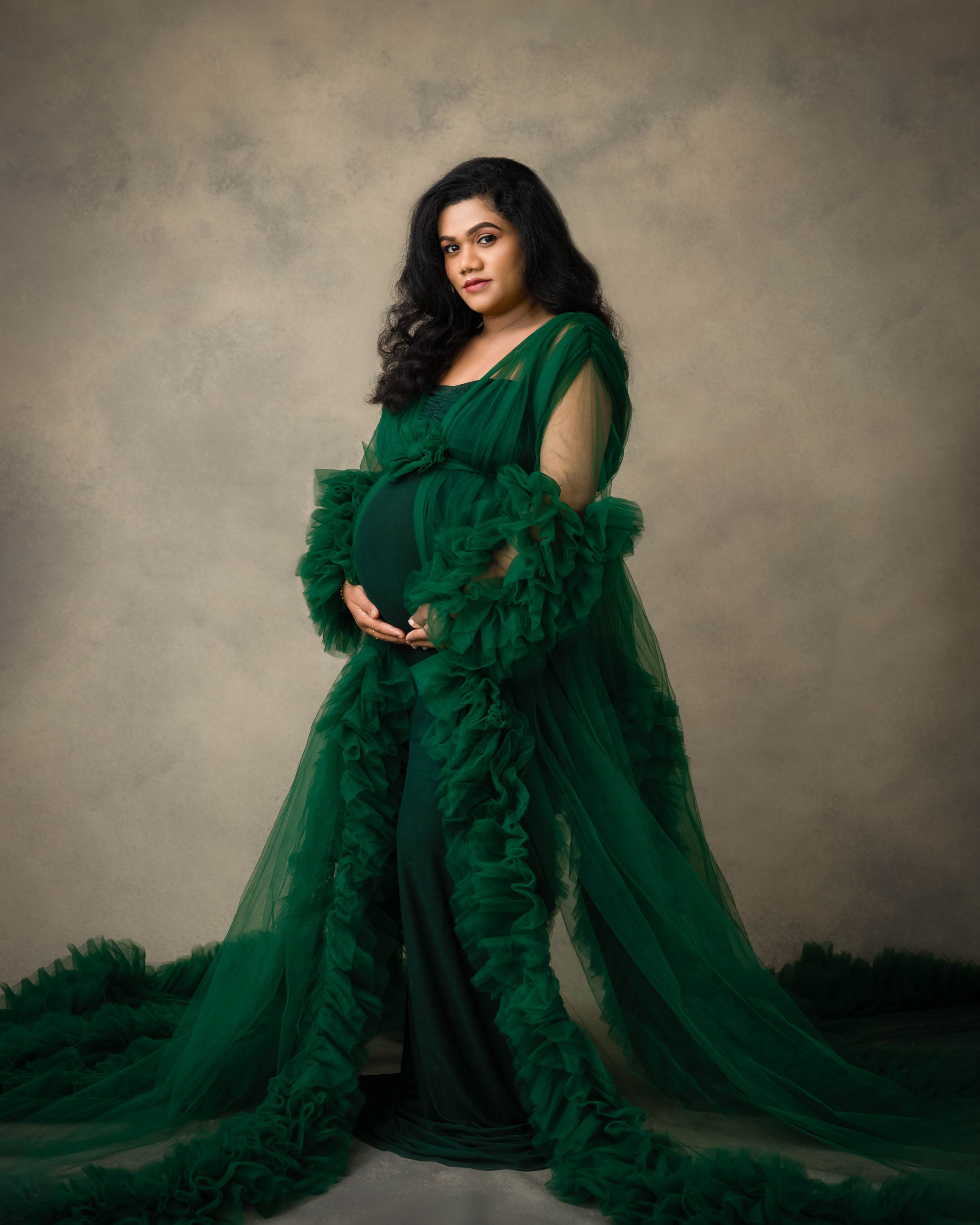 Elegant maternity portrait featuring a flowing emerald green tulle gown against a muted backdrop.