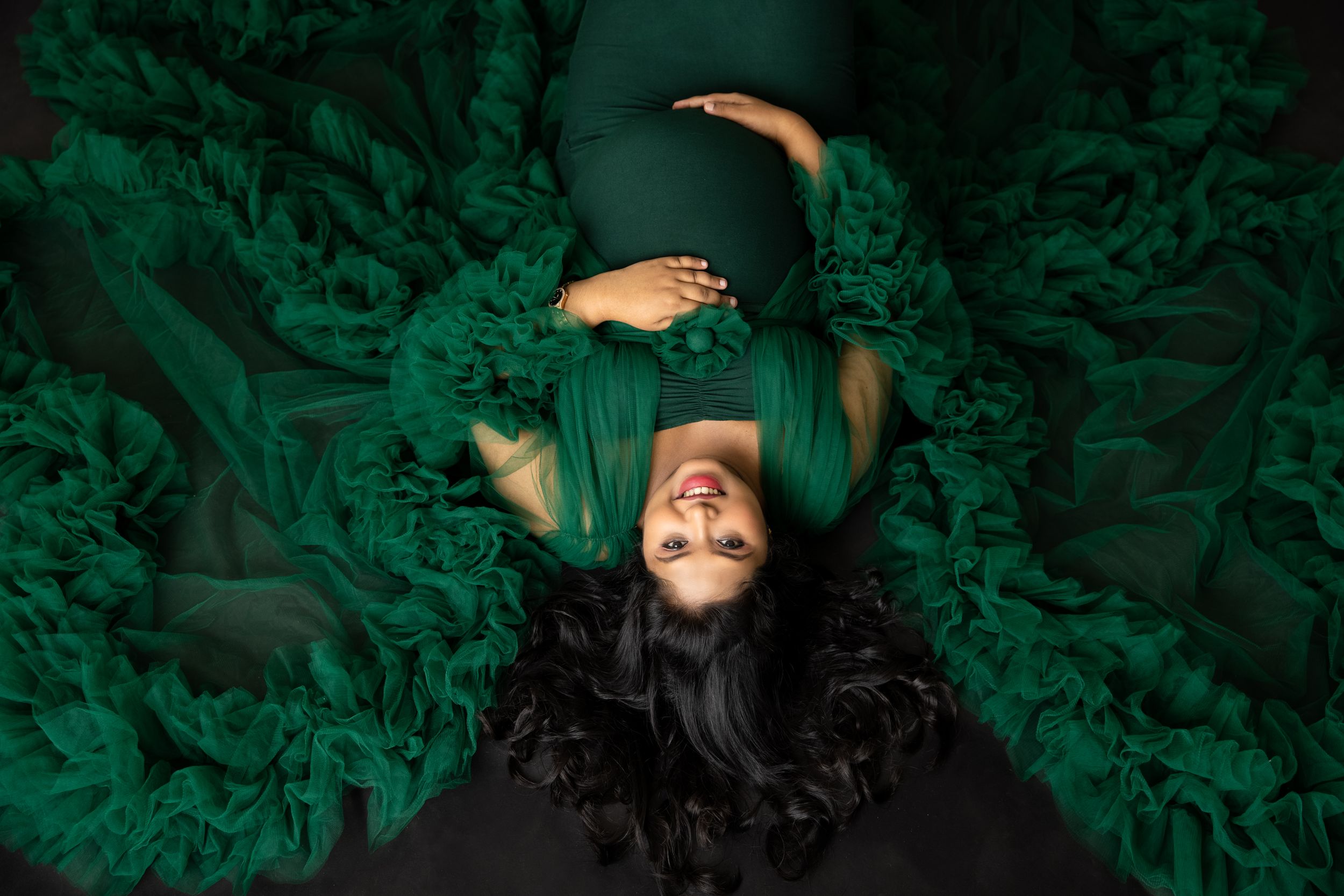 Overhead view of maternity portrait with subject lying in swirling emerald green fabric.