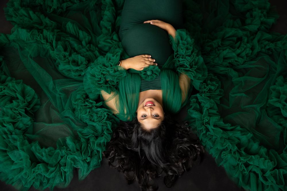 Overhead view of maternity portrait with subject lying in swirling emerald green fabric.