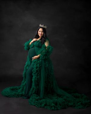 Dramatic maternity photo with flowing emerald green tulle gown and crown against dark background.