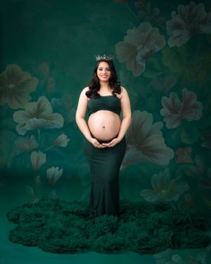 Maternity portrait with emerald green floral backdrop showing an expecting mother in a dark formal gown.
