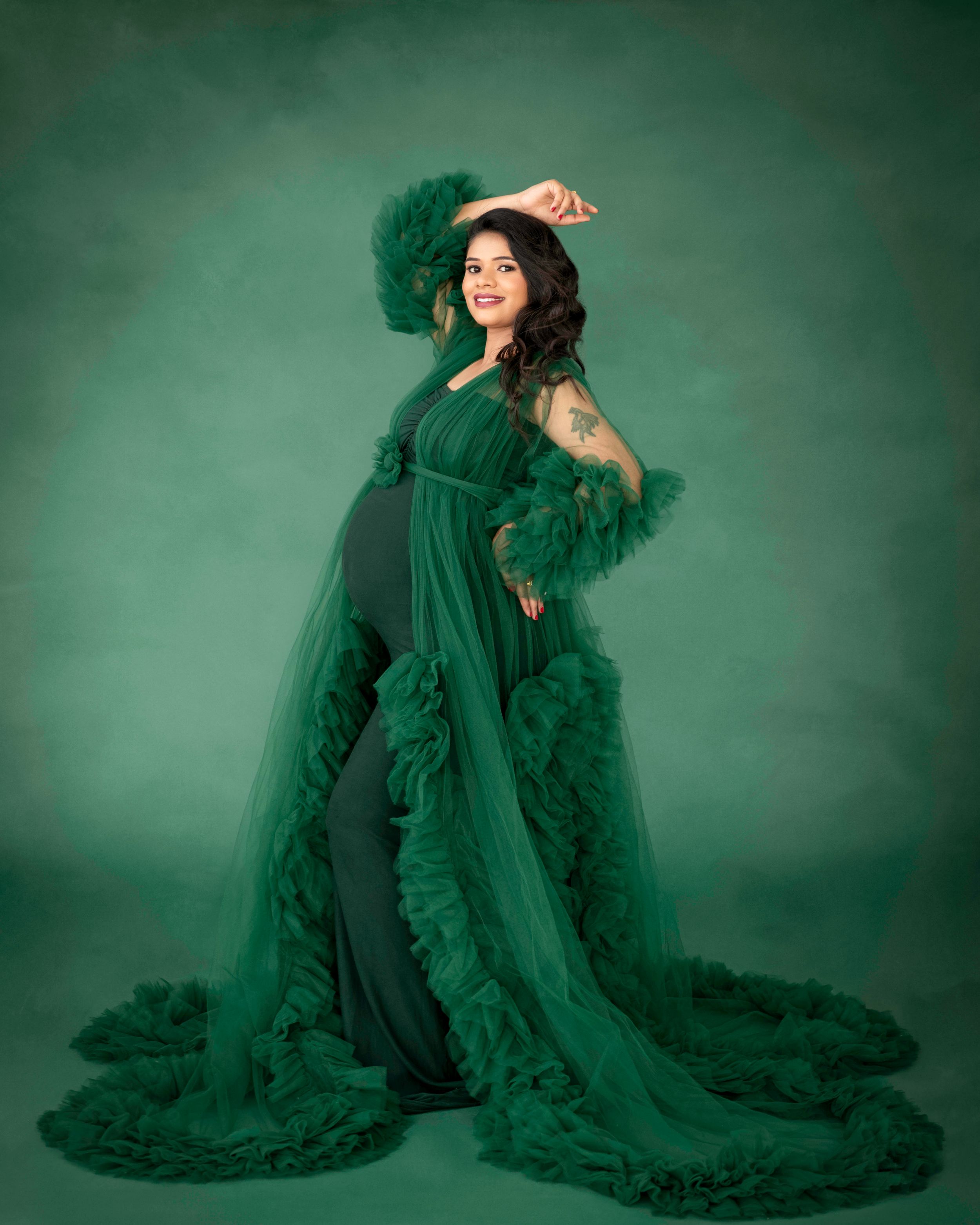 Maternity portrait with dramatic emerald green ruffled gown against matching background.