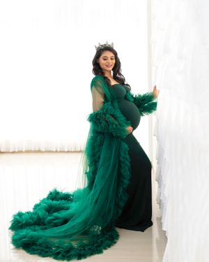 Maternity portrait featuring a flowing emerald green tulle gown with feathered details.