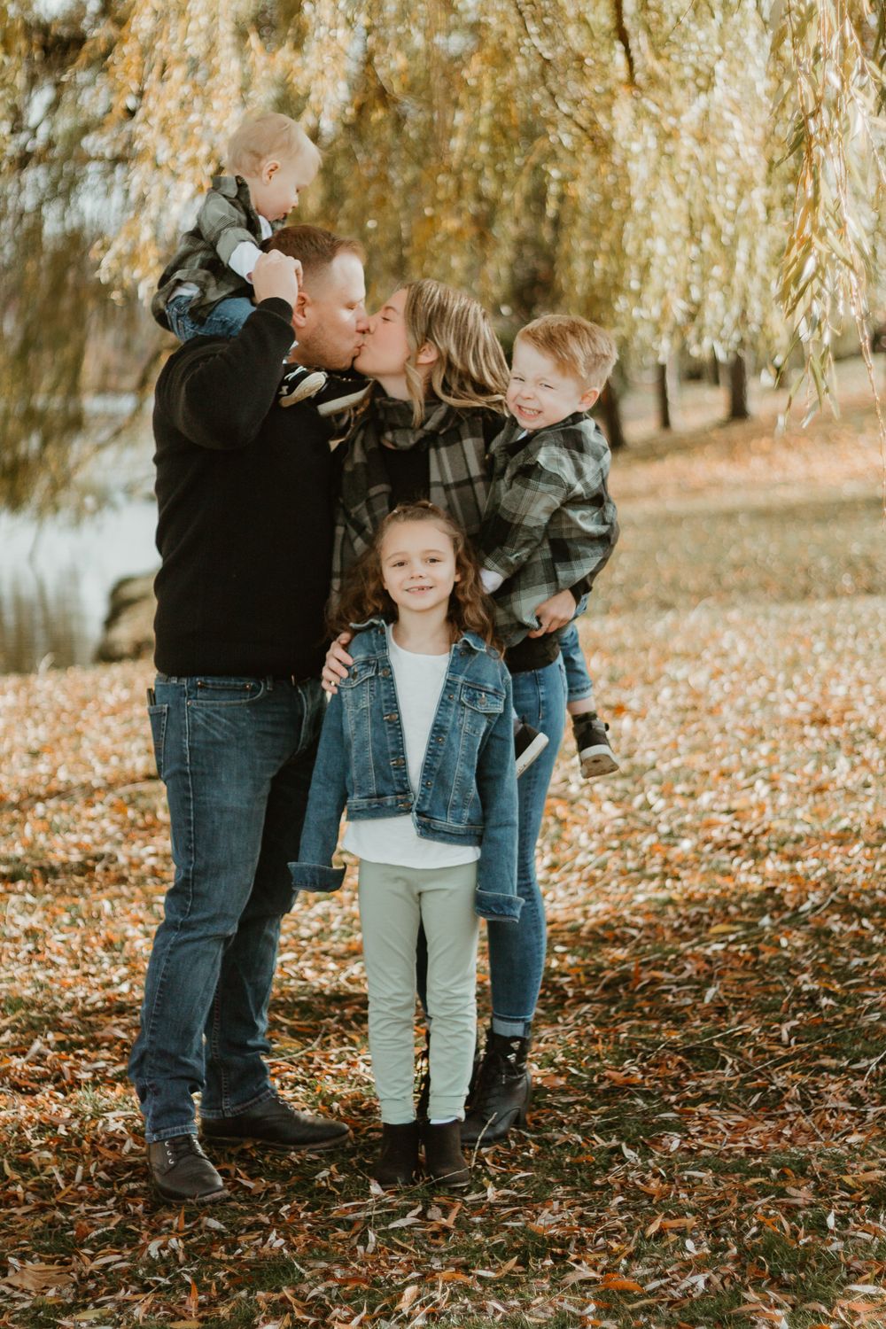 A family shares playful moments together on ground covered with autumn leaves.