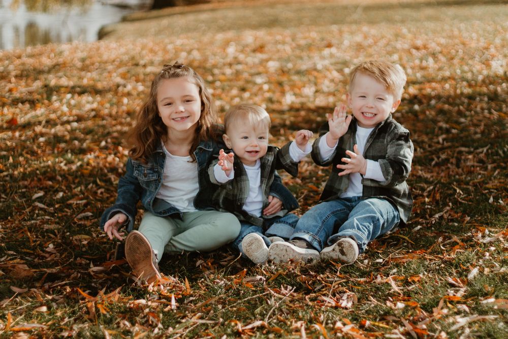Children playing and laughing together while laying in colorful fall leaves.