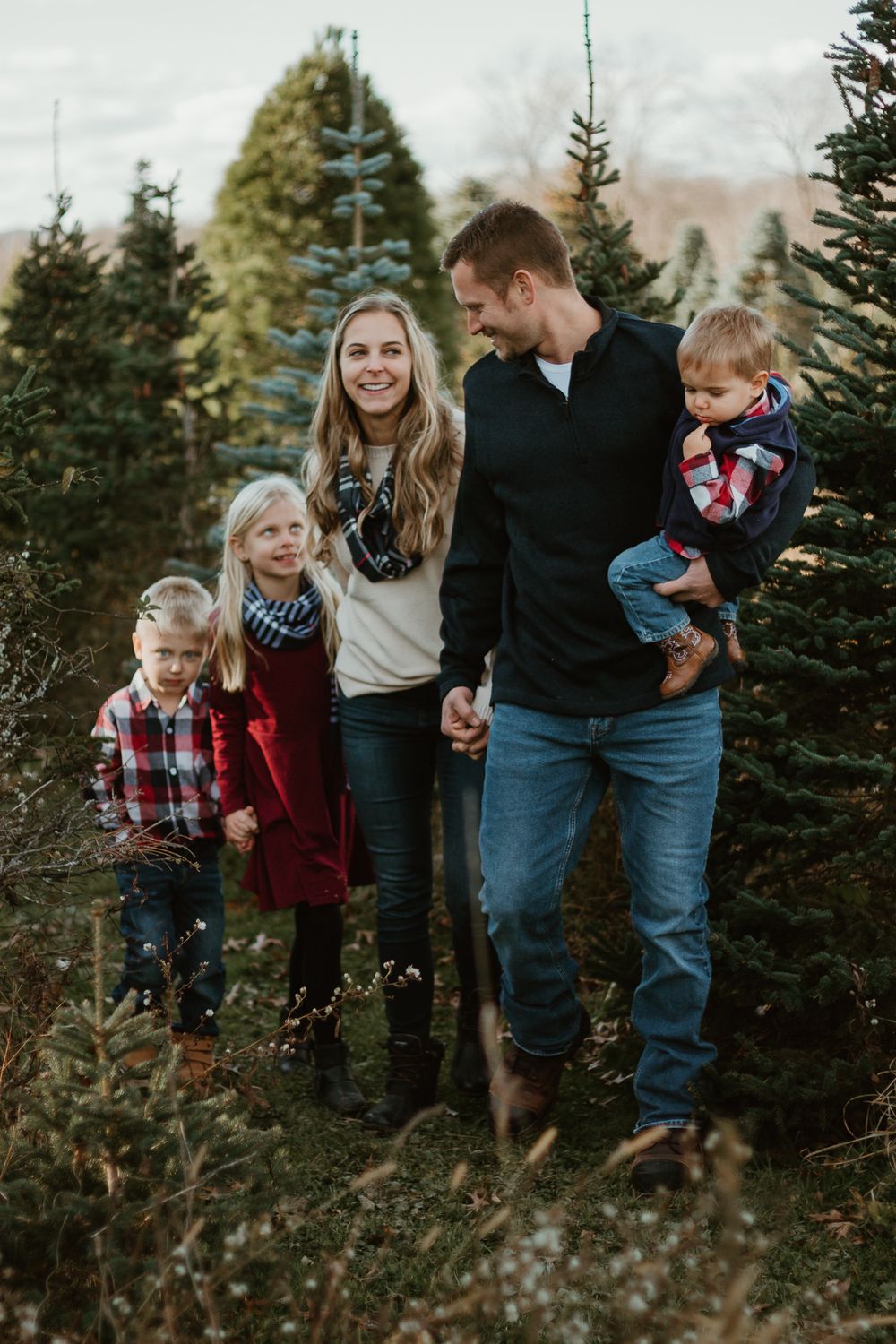 Candid family moments captured between evergreen trees in natural lighting.