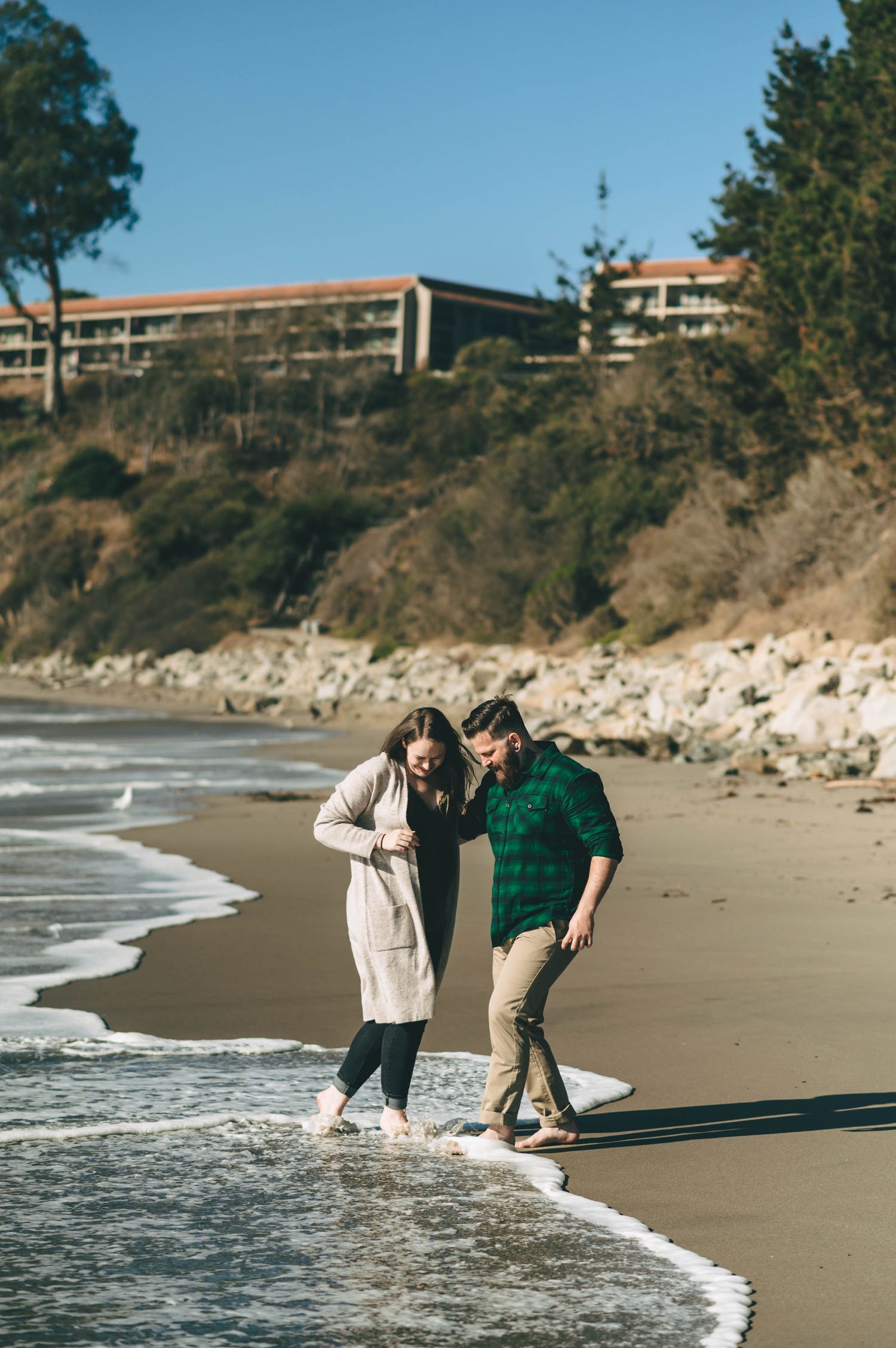 Couple playing in the waves at the beach near coastal cliffs.