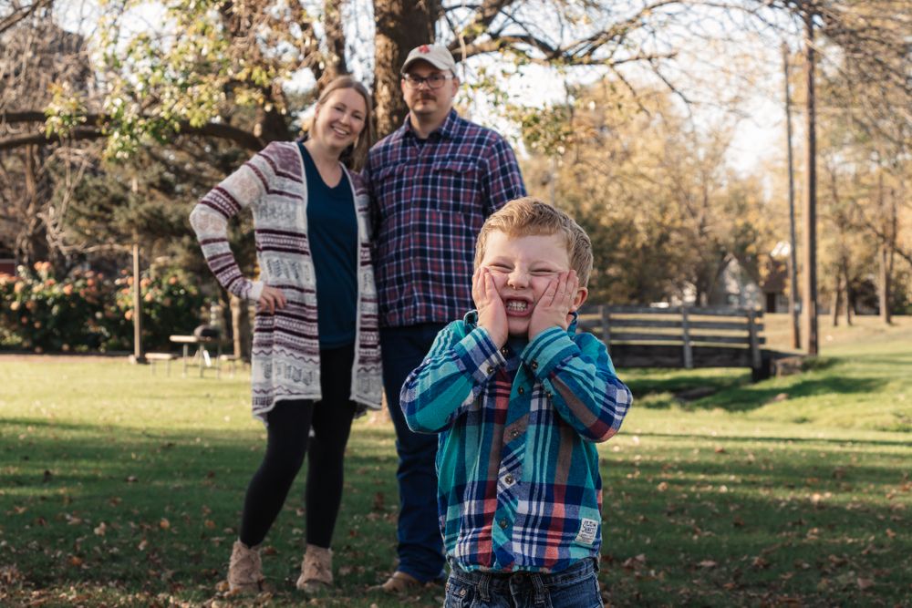 A young child makes a funny face while playing outdoors with parents in autumn.