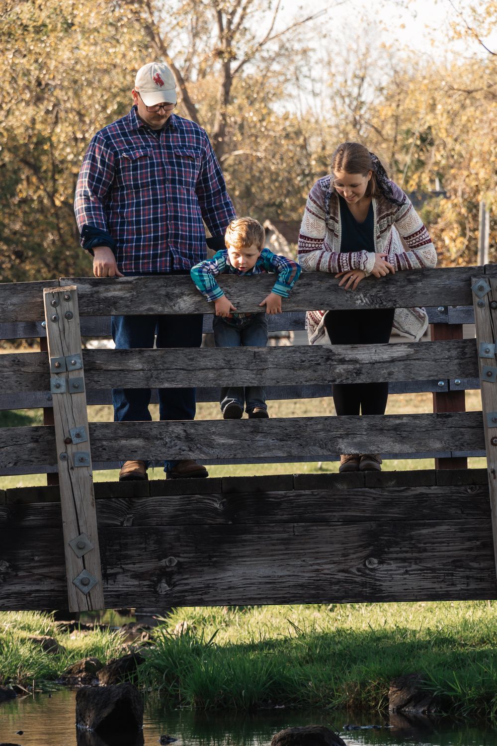 A family spends time together on a wooden bridge overlooking a pond on an autumn day.