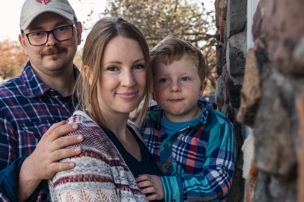A cozy family photo taken outdoors with matching plaid shirts and autumn scenery.