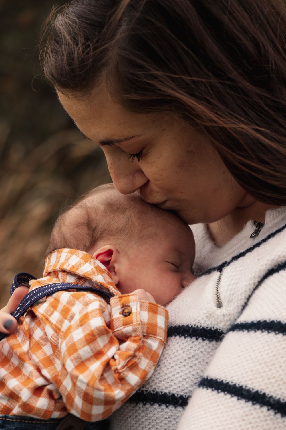 Intimate moment between parent and sleeping infant in striped sweater and plaid clothing.