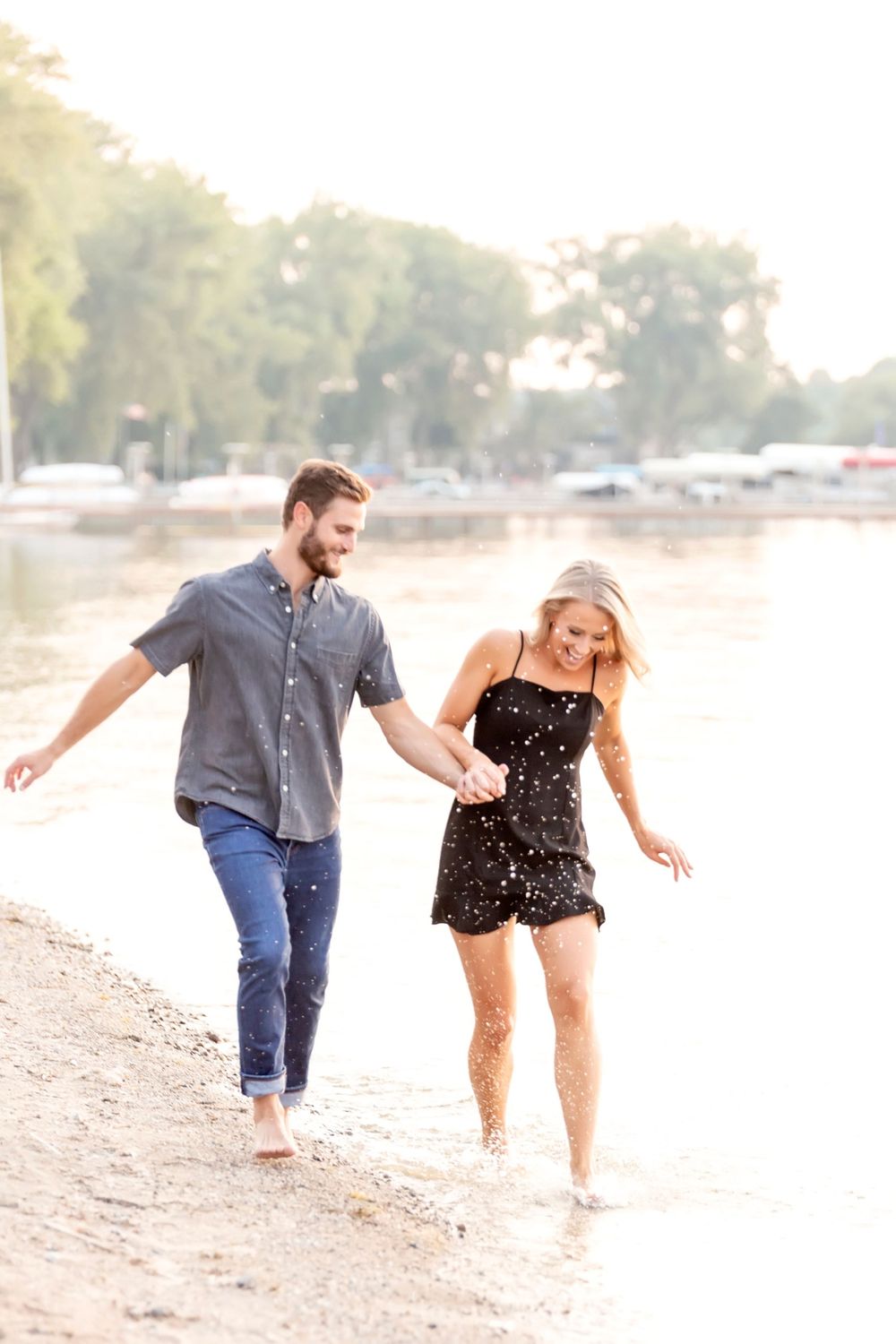 Playful couple walking and laughing together along a beach shoreline.