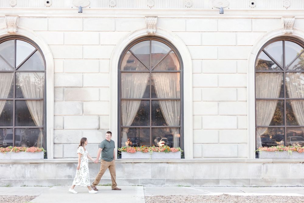 A couple walks together past arched windows on a classic stone building exterior.