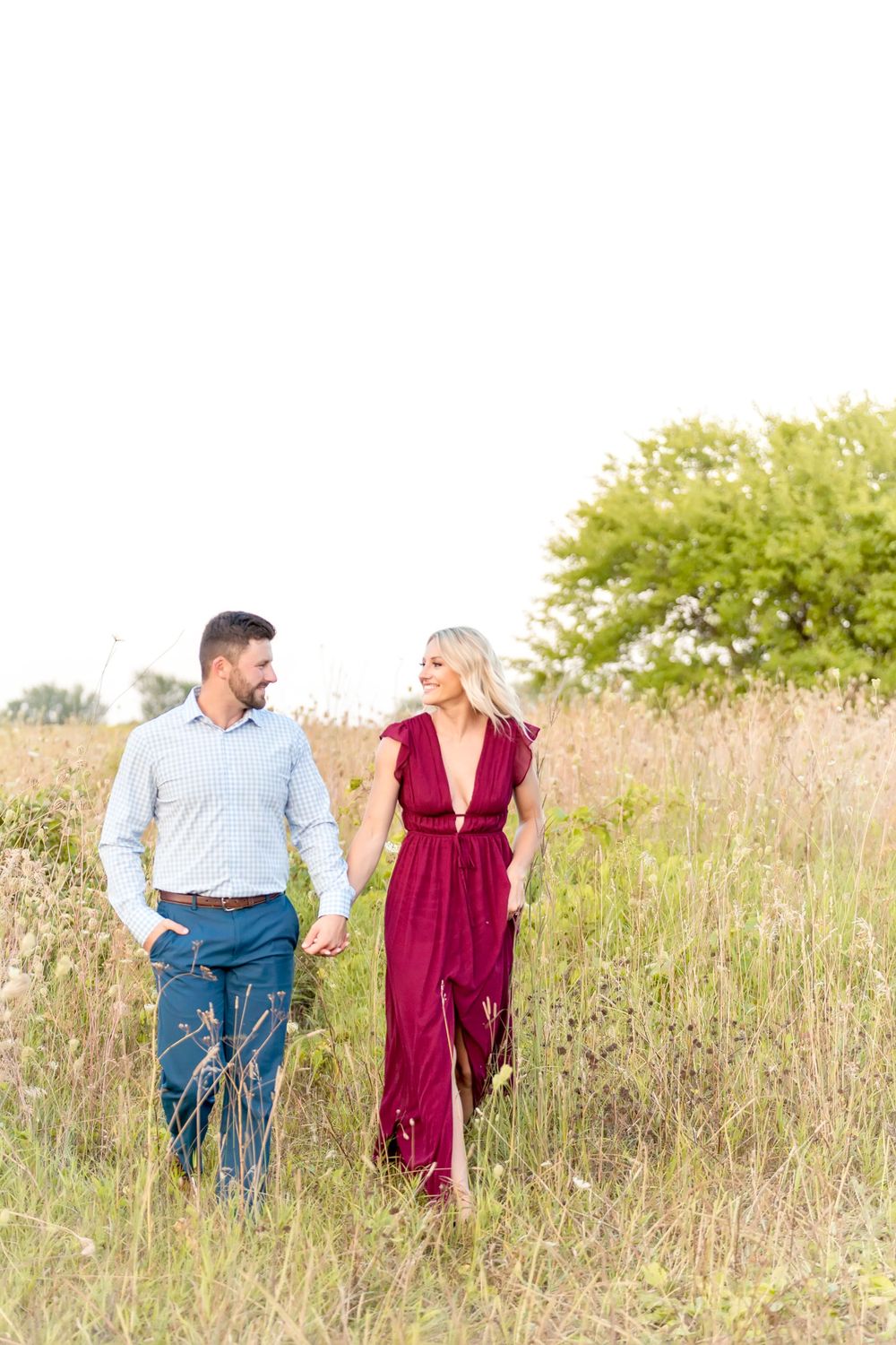 A couple walks hand in hand through a scenic field of tall grass in summer.
