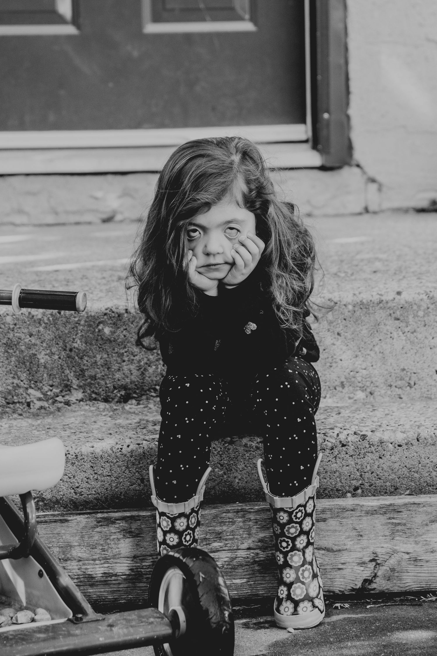A playful black and white portrait sitting on steps wearing patterned rain boots.
