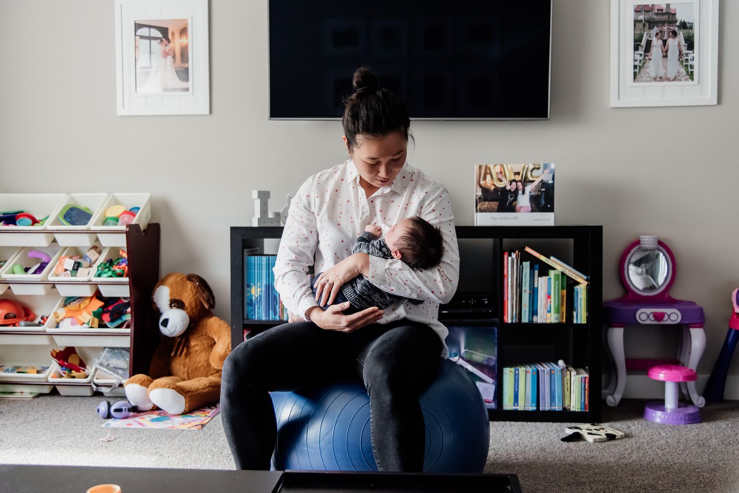 Nursing parent sitting in a blue chair in a nursery room with toys and books visible.