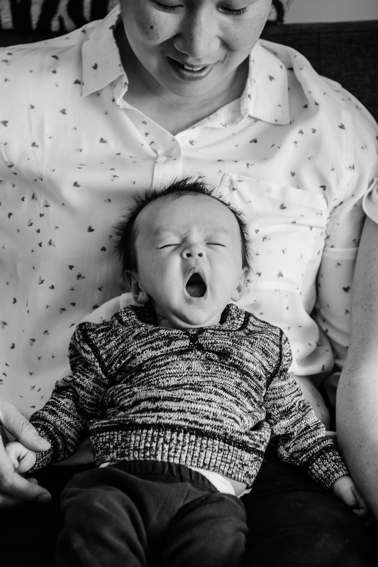 Black and white photo of an infant yawning while wearing a knit sweater.
