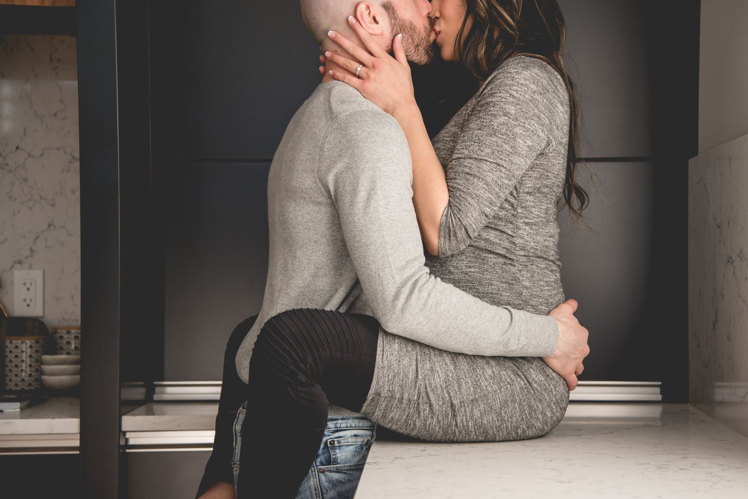 An intimate moment between a couple wearing gray sweaters in a dimly lit room.