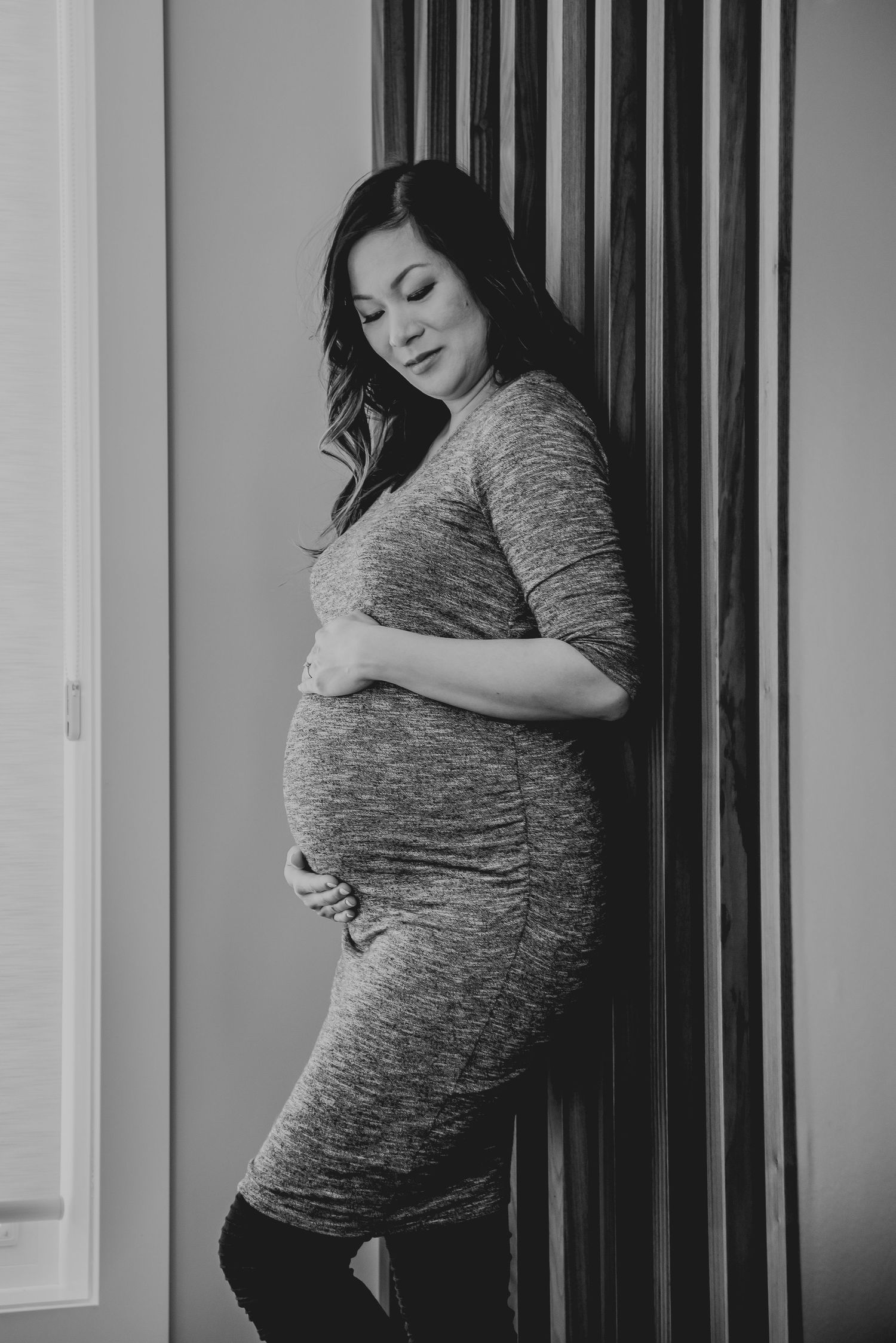 A side profile maternity portrait in a gray dress against striped wall panels.