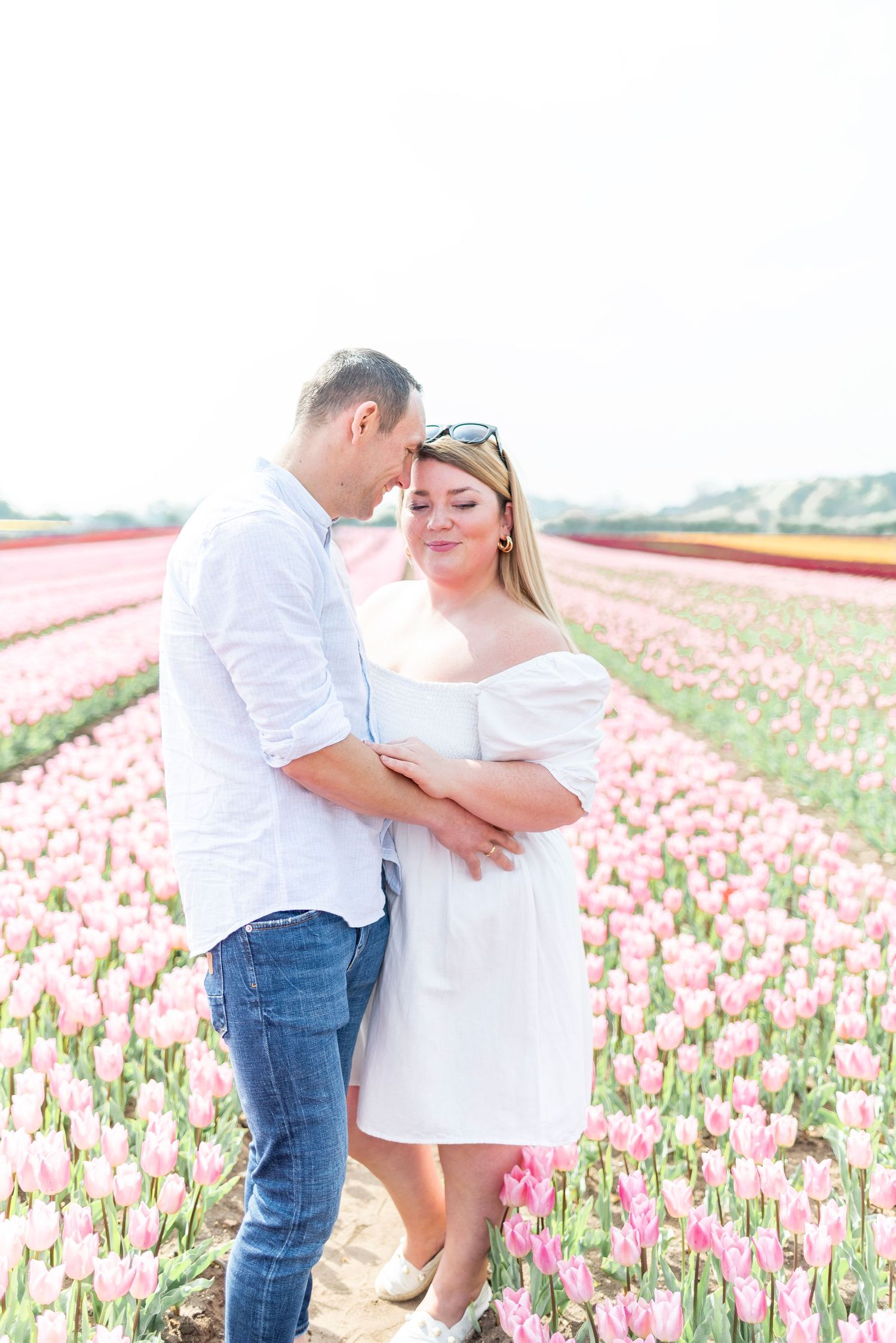 Romantic couple in white embracing in a field of pink tulips on a sunny day.