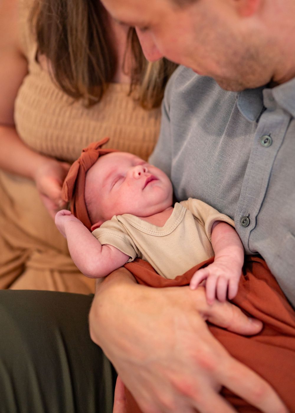 A tender moment showing a newborn baby in tan clothing being cradled with care.