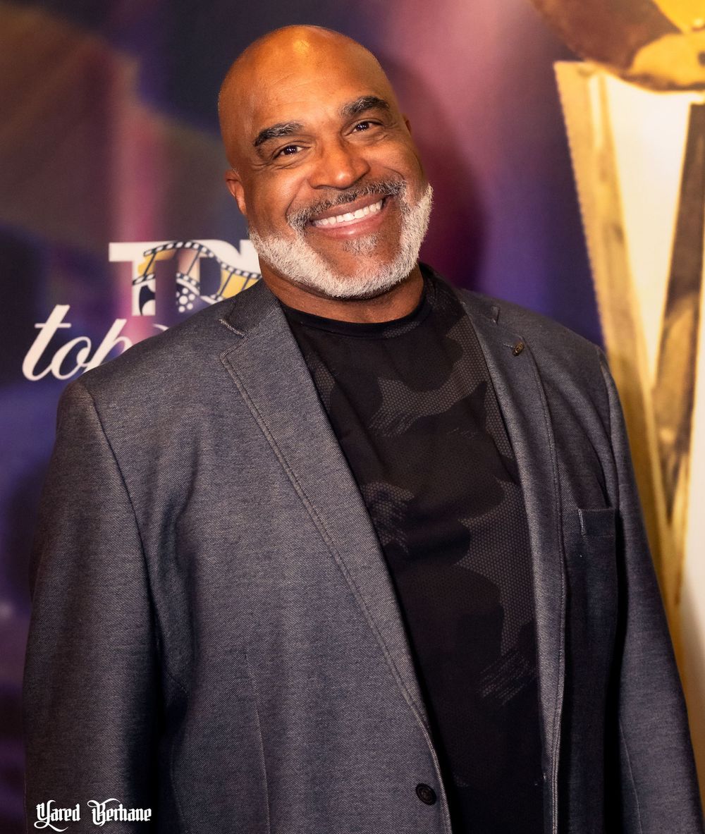 A smiling person in a dark blazer poses at an entertainment industry event.