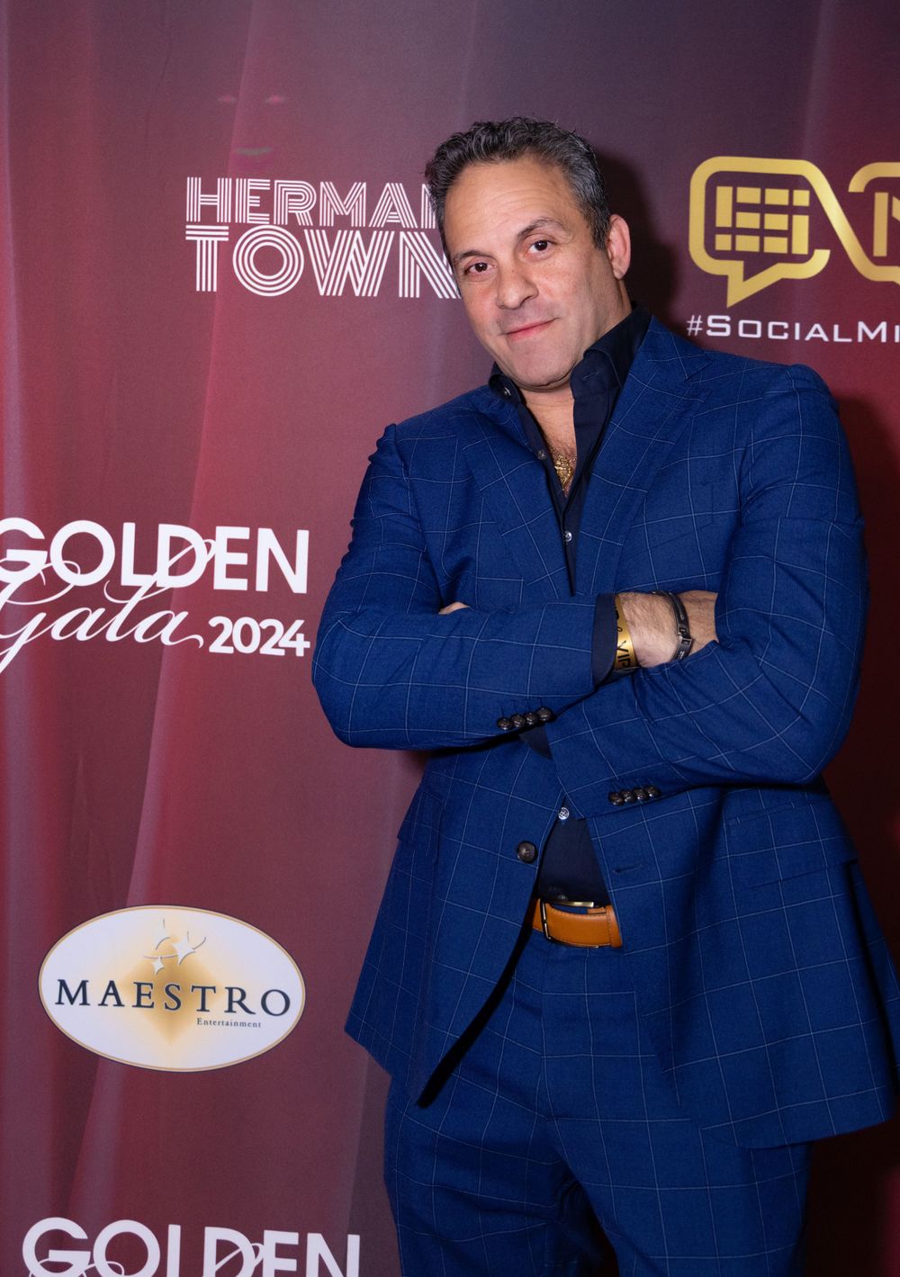 A person in a blue suit poses at the Golden Gala 2024 event with arms crossed.