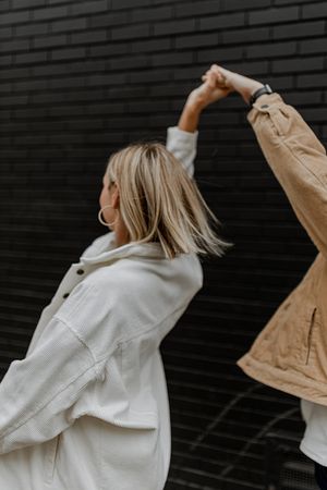 Dancing couple in white and tan jackets against dark wall with raised arms.