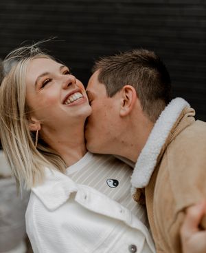 Intimate romantic moment captured against dark wall background with white and tan outfits.