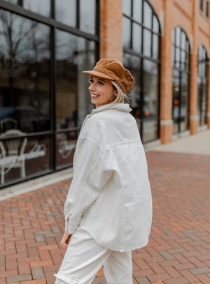 Stylish winter street fashion pose in all-white outfit with tan newsboy cap.
