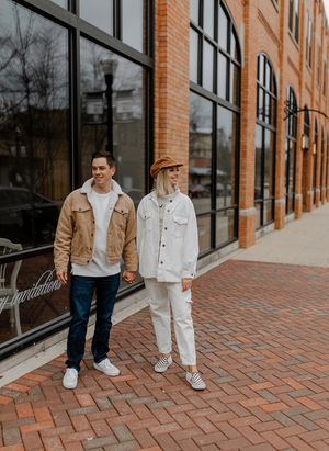 Couple in coordinating casual outfits standing on brick sidewalk by modern building.