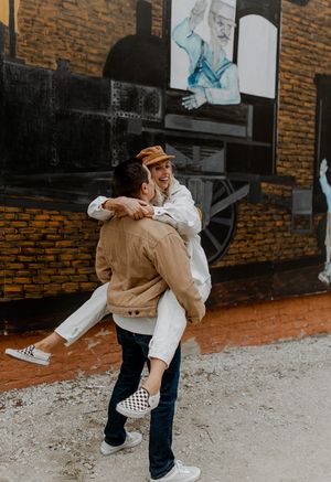 Playful couple in coordinated outfits sharing fun moment outside brick building.