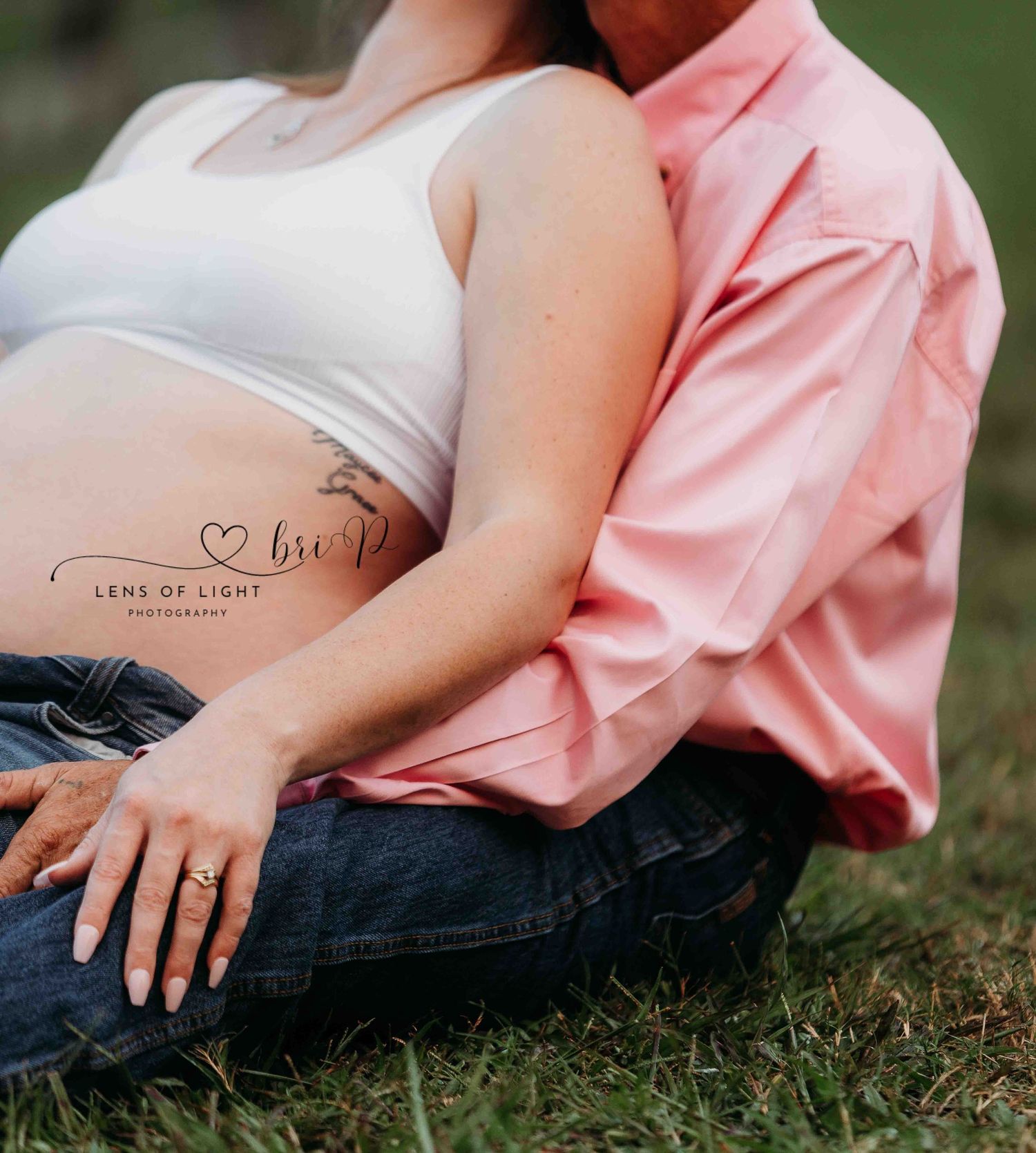 An intimate maternity photo showing hands resting on a pregnant belly outdoors.