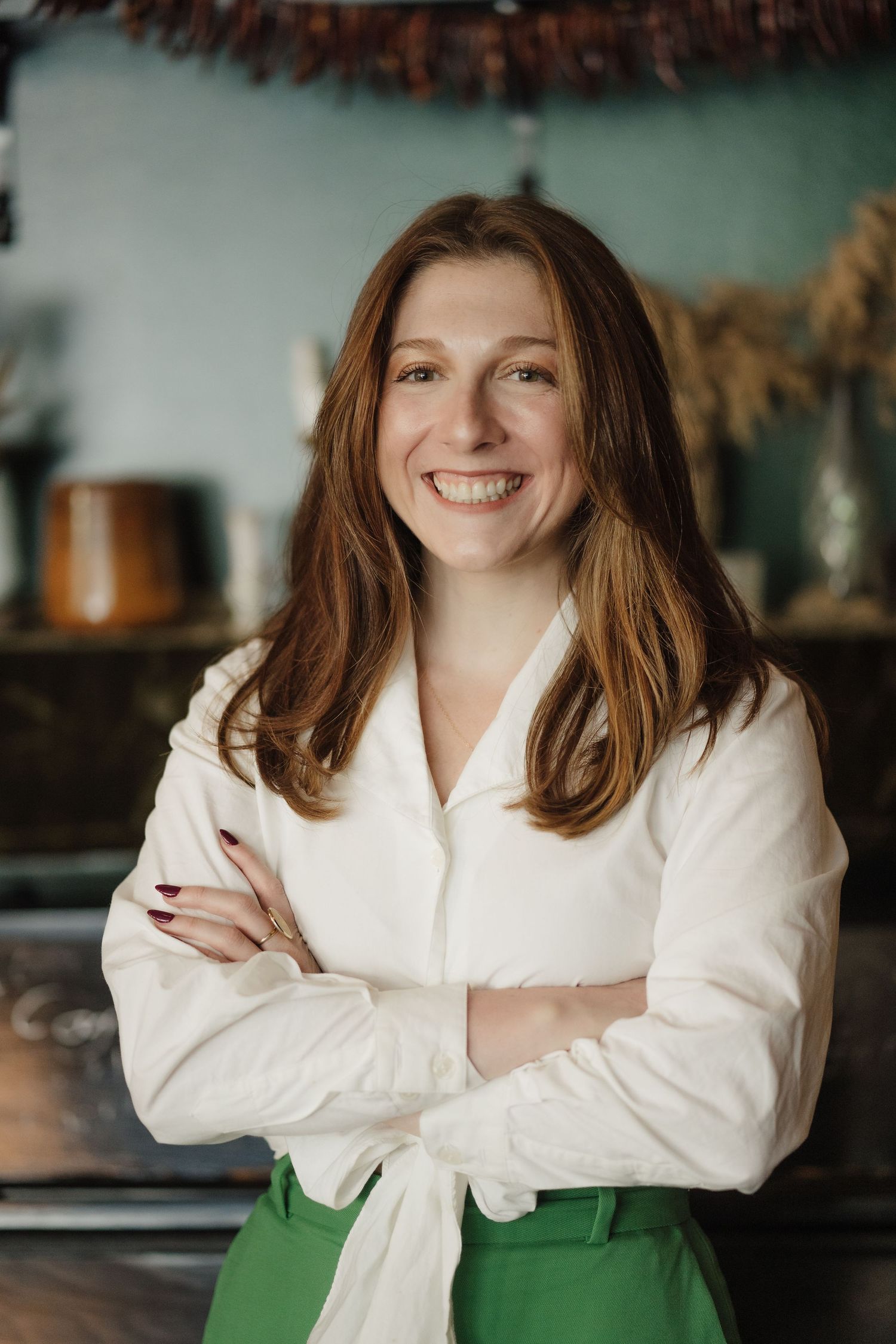 Professional portrait in white top and green pants in cozy interior setting.