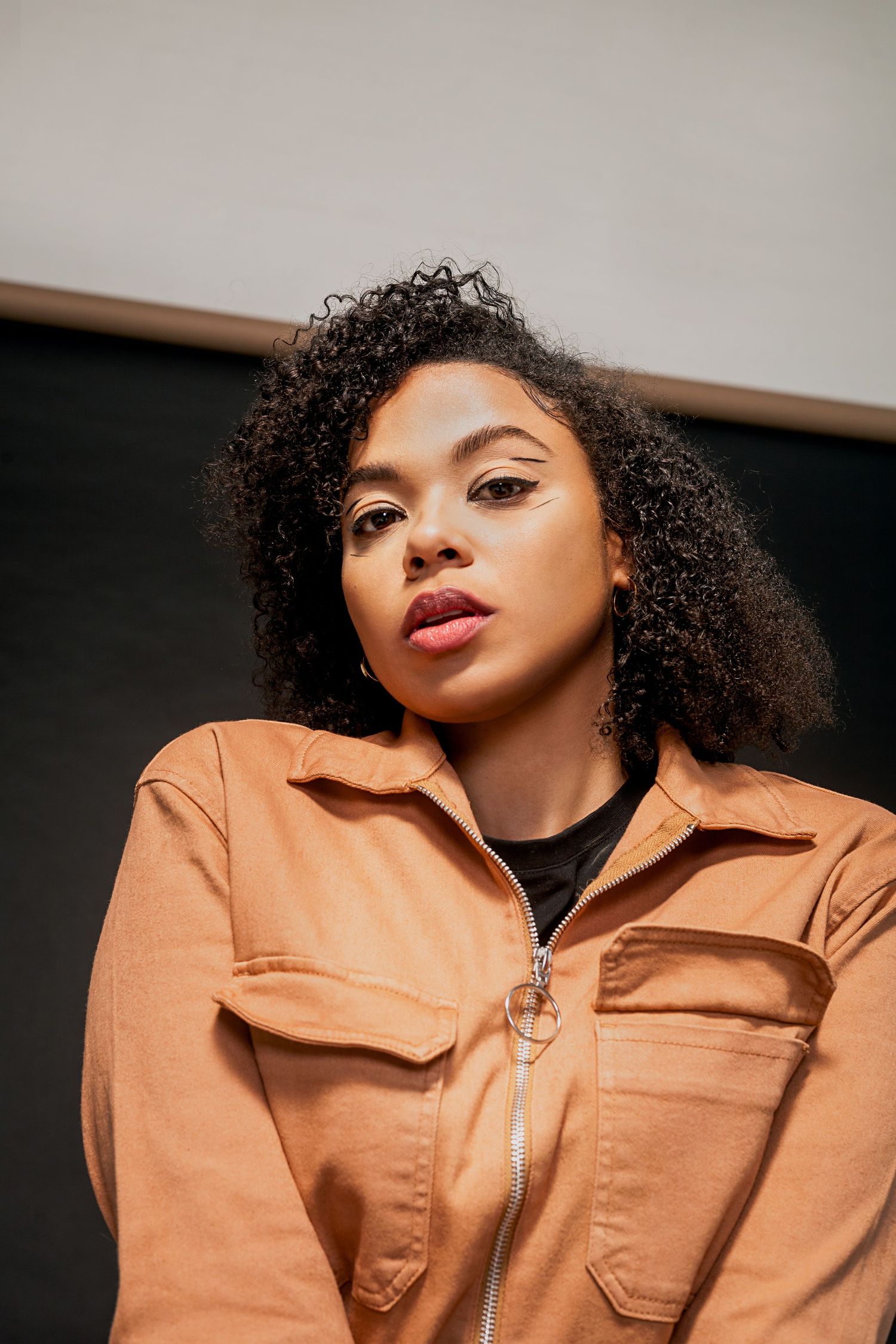 Close-up fashion editorial showing natural curly hair and caramel-colored utility jacket.
