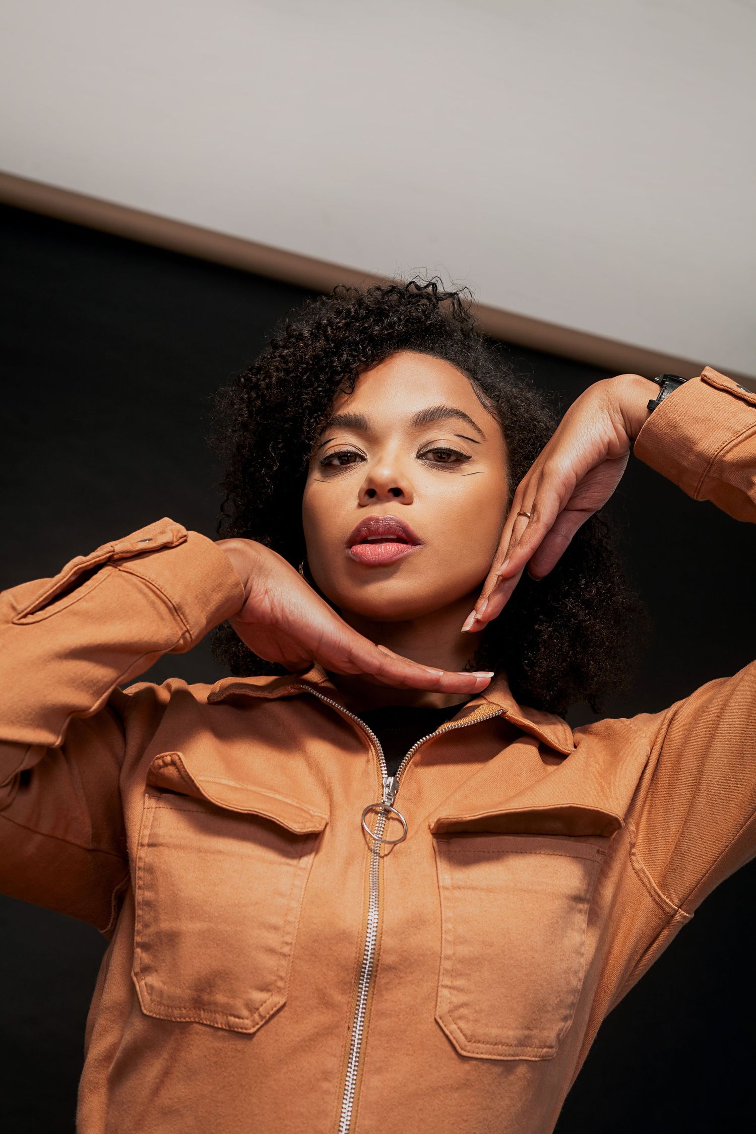 Fashion portrait featuring a tan zip-up jacket with utility pockets against a dark background.
