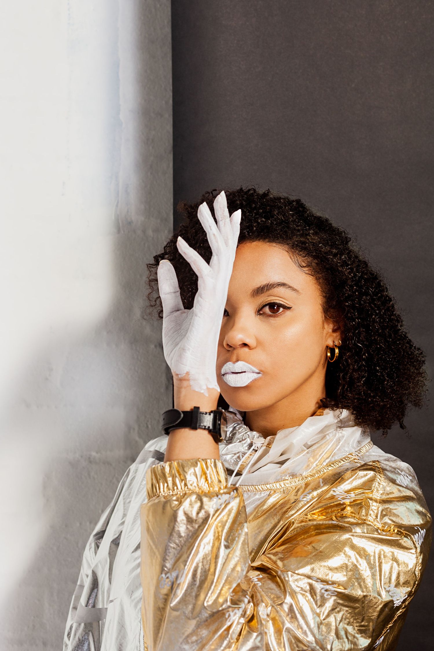 Studio fashion shot with gold metallic jacket and white gloves against neutral background.
