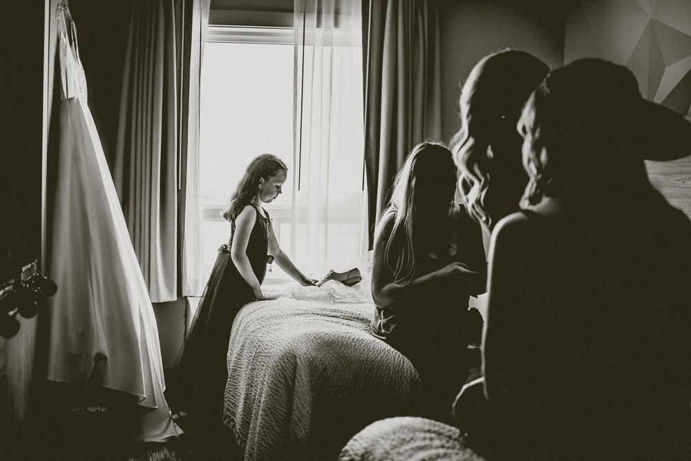 Black and white image showing preparations in a sunlit room with curtains and silhouettes.