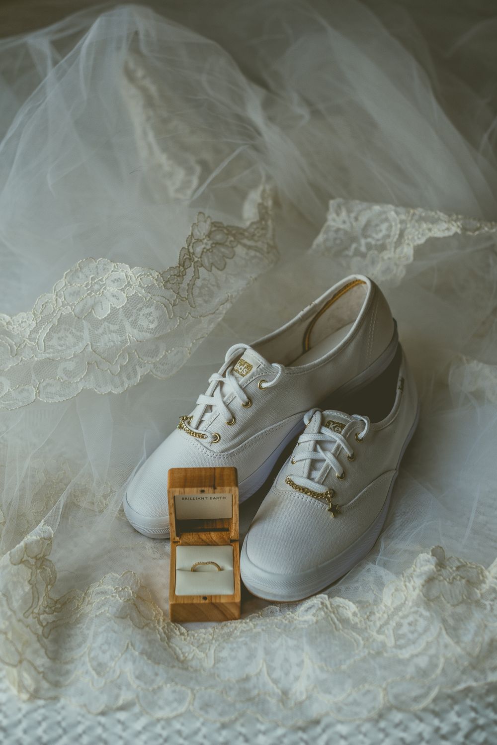 White wedding sneakers and gold ring box displayed on delicate lace veil.