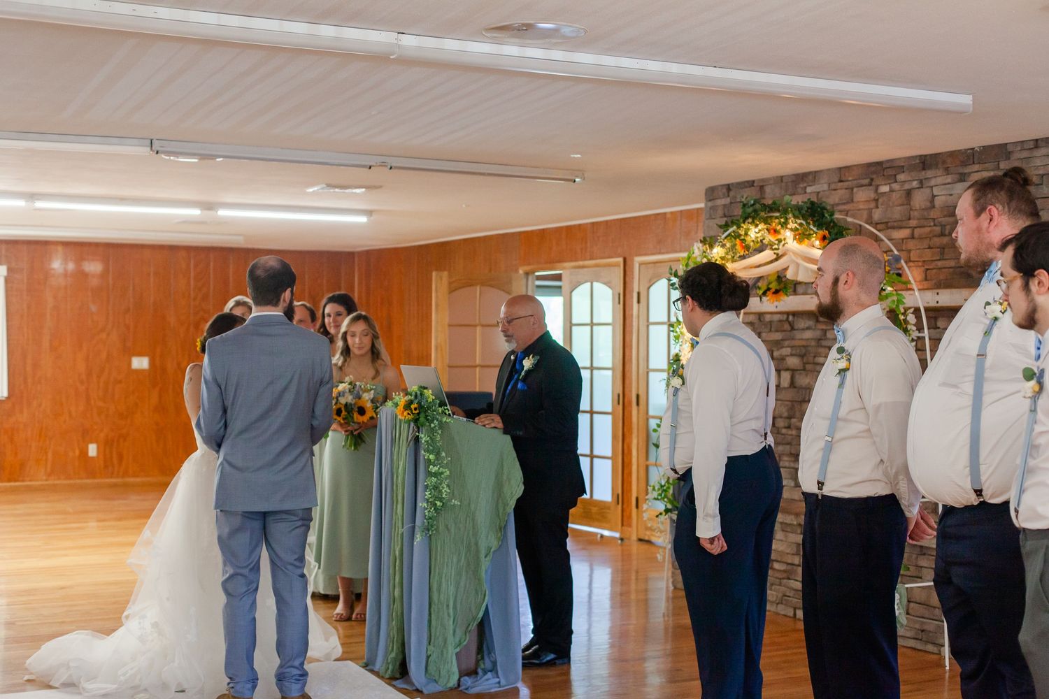 Wedding guests and bridal party mingling in a wood-paneled reception hall.