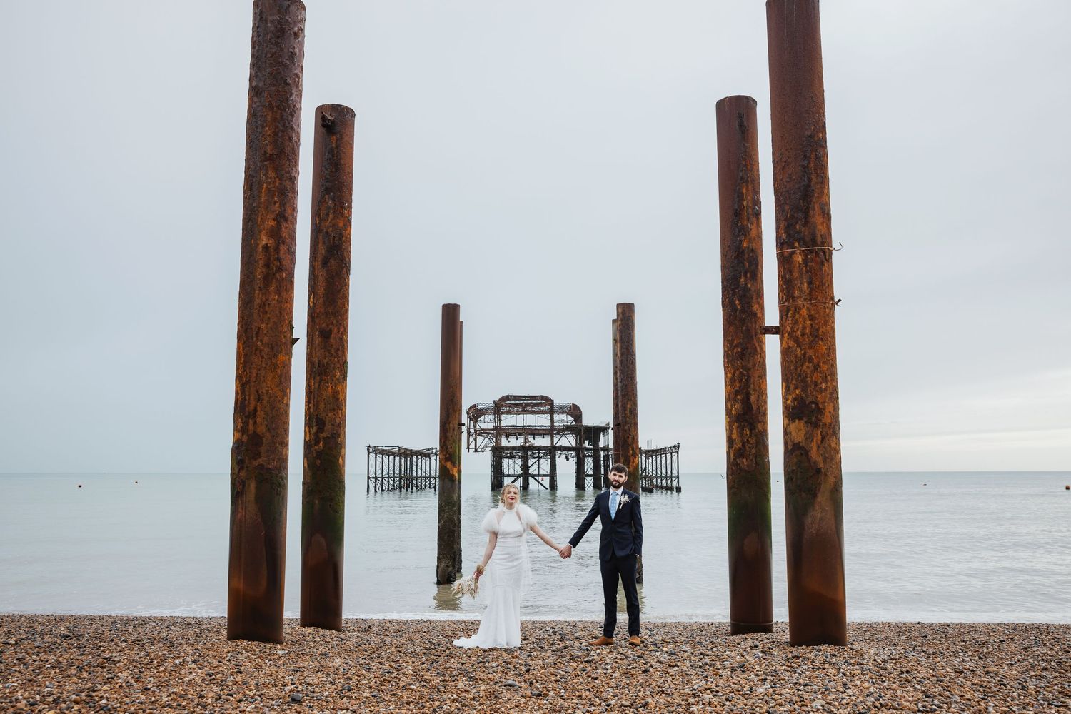 newly wed couple holding hands in front of the Brighton West Pier on the beach