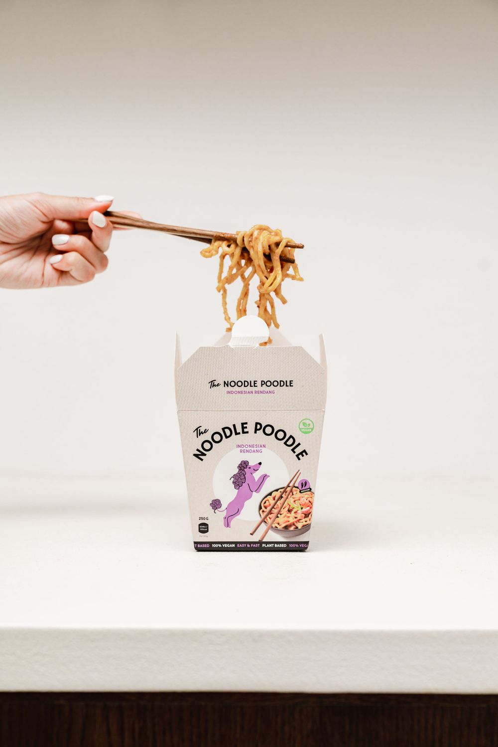 Chopsticks lifting noodles from a Noodle Poodle takeout container.