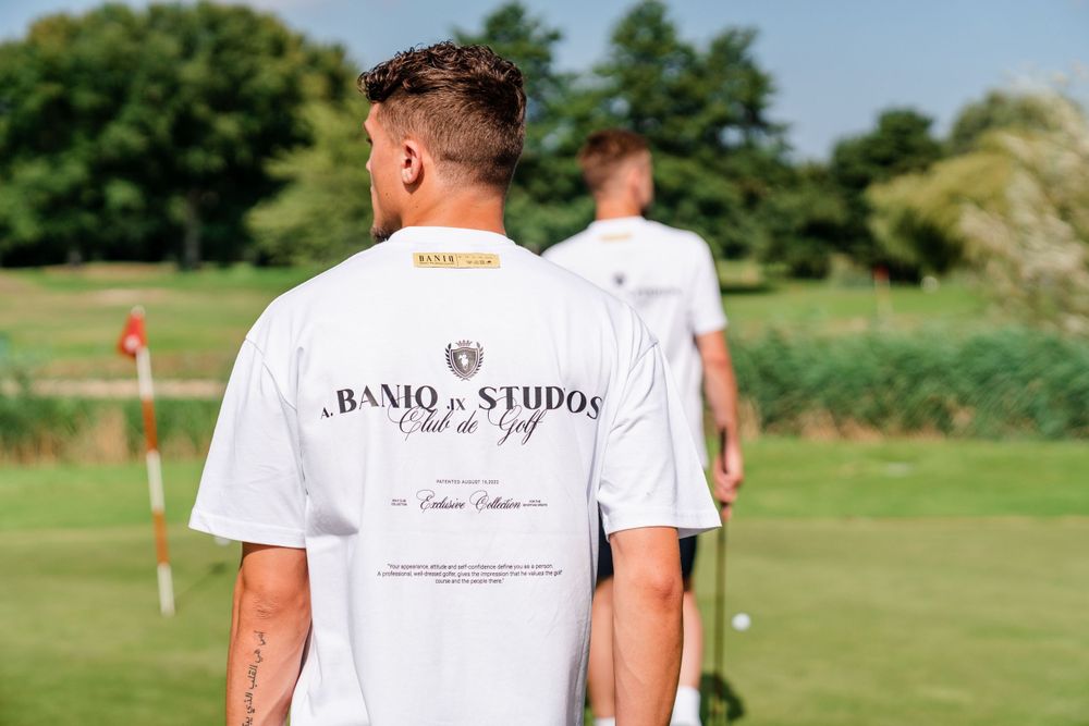 Two golfers in white t-shirts stand on a sunny golf course with lush green surroundings.