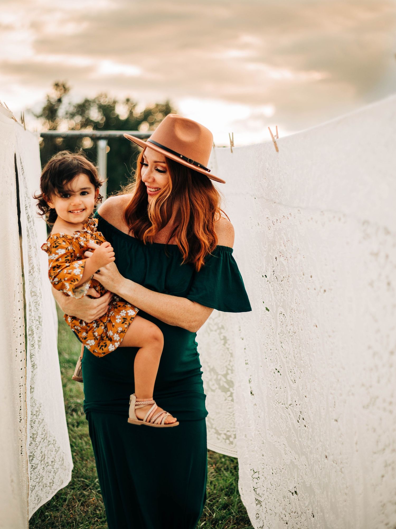 Lifestyle portrait of parent and child in casual attire against white wall outdoors.